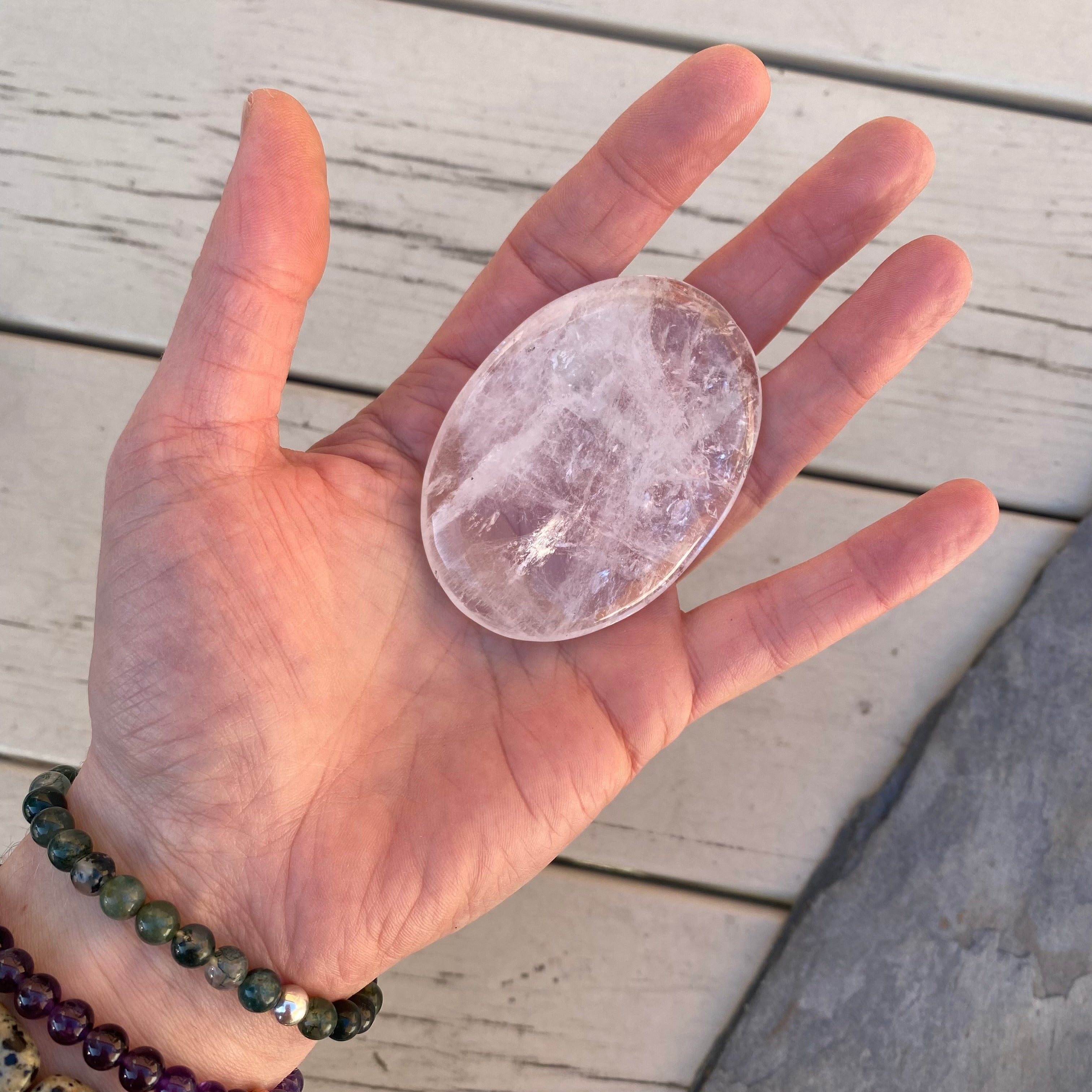 A flat oval Glassy crystal, clear in places with fracture within that catch the light with a milky appearance and spark in places. Quartz Palmstone Gemstone