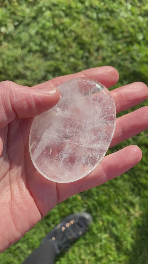 A flat oval Glassy crystal, clear in places with fracture within that catch the light with a milky appearance and spark in places. Quartz Palmstone Gemstone